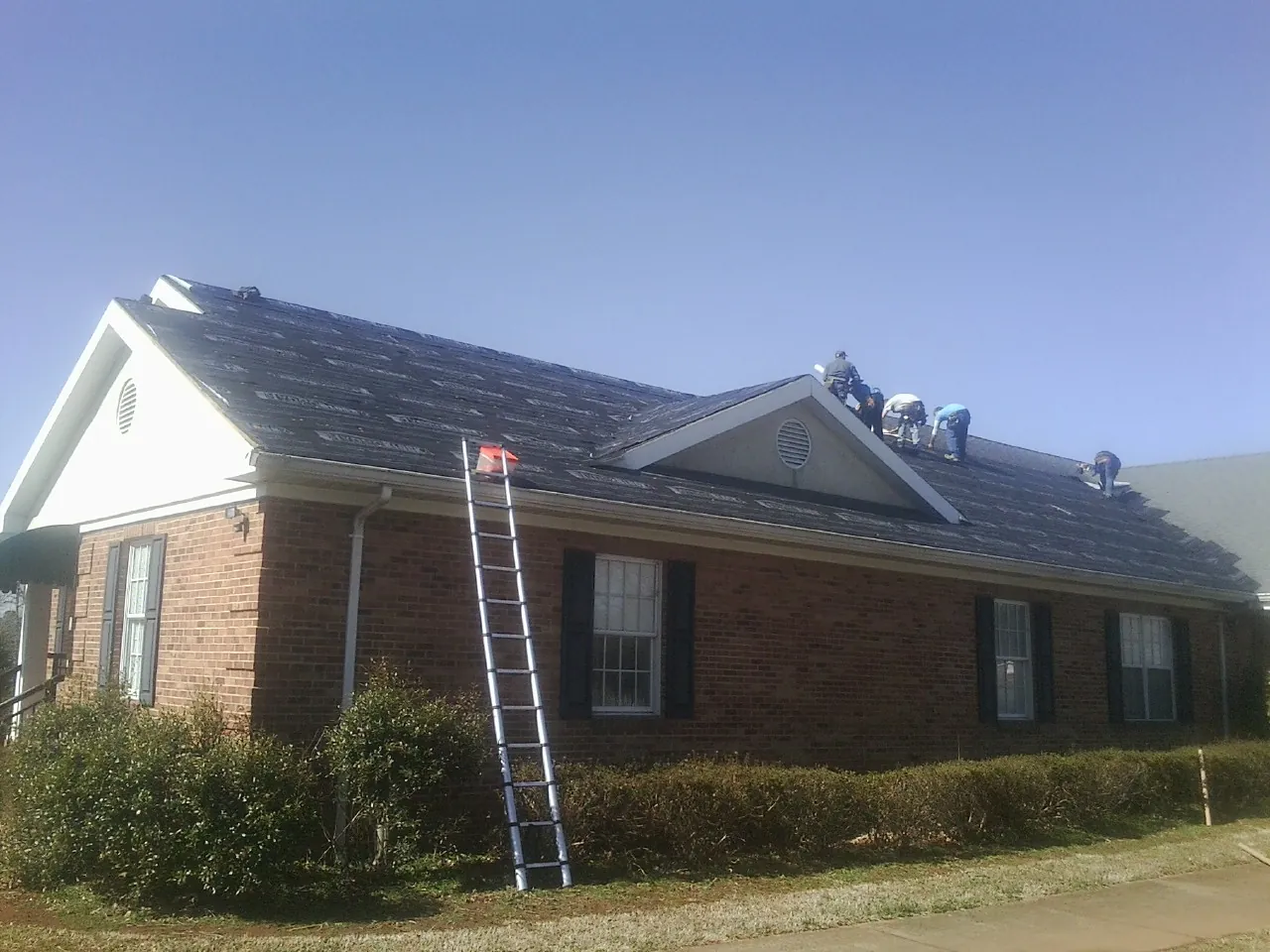 Crew tearing shingles off a brick ranch roof with a ladder set — Emergency Roof Repair work by our crew in Beavertown