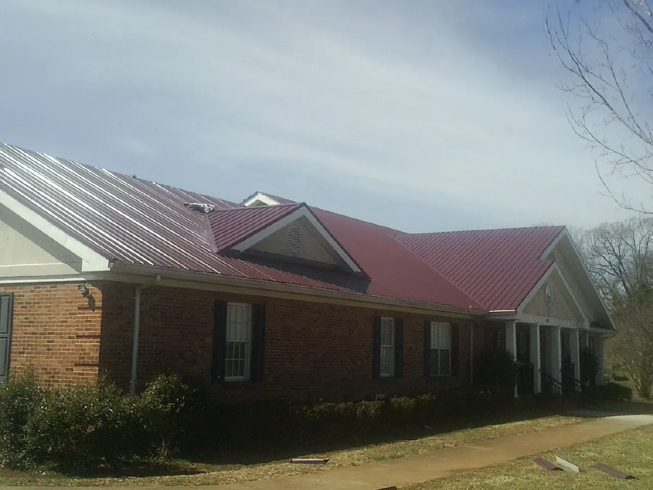 Red metal roof with gabled entries on a long brick building, from a Hail Damage Roof Repair job in Beavertown