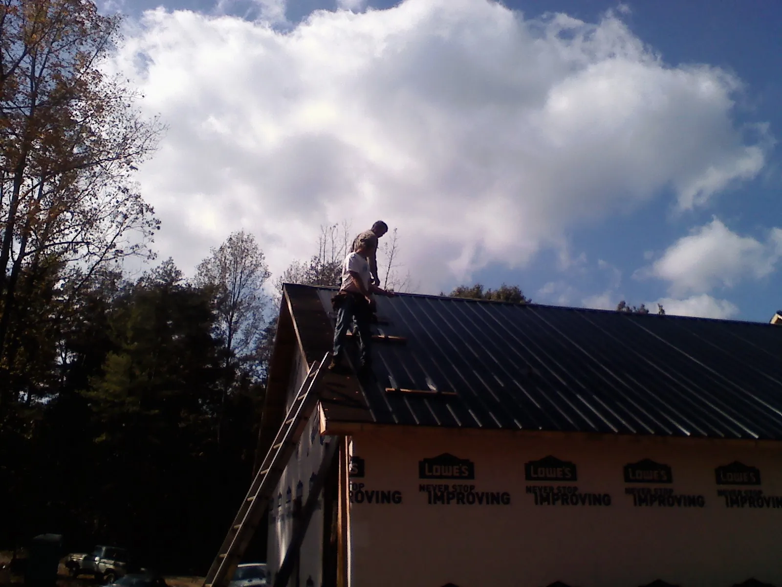 Roofer fastening dark metal panels high against a cloudy sky, from a Roof Inspection job in Beavertown