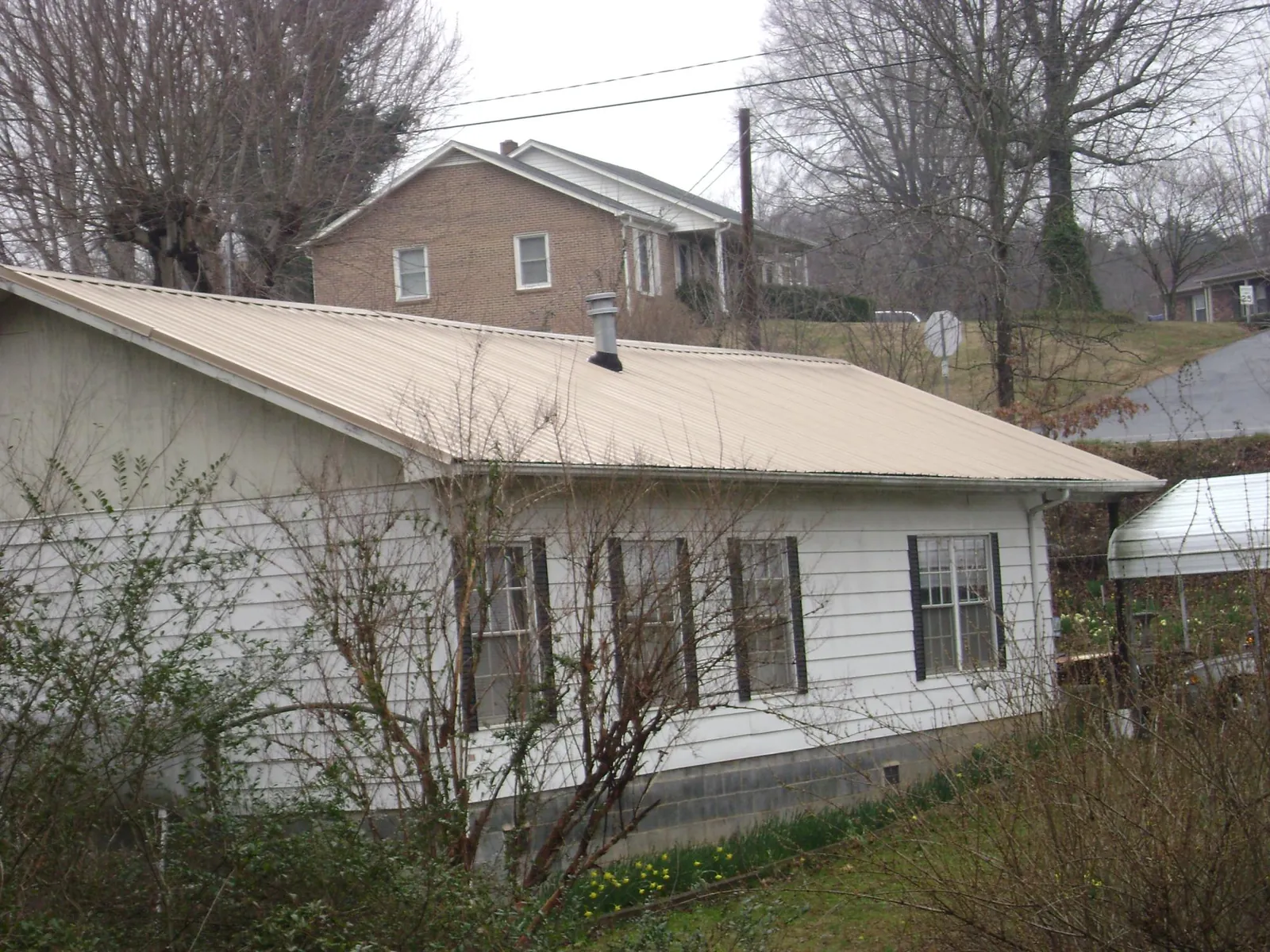 Tan metal roof on a white sided house set into a hillside — Commercial Roofing by Roofing Brothers in Beavertown